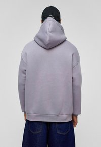 Paarse oversized hoodie met een grote capuchon, ribbels aan de mouwen en zoom, en een gladde katoenstructuur. Gecombineerd met losse donkere spijkerbroek.