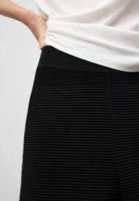 Jupe noire côtelée en tissu texturé avec une taille élastique, ornée de rayures verticales et d'un bord supérieur lisse.