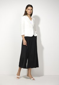 White textured blazer with a single button, paired with loose black culottes and white open-toe heels. Simple, modern silhouette.