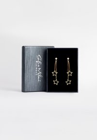 Boucles d'oreilles en forme d'étoile dorée avec un design en chaîne, comportant une petite pierre claire en haut. Présentées dans une boîte doublée de velours noir.