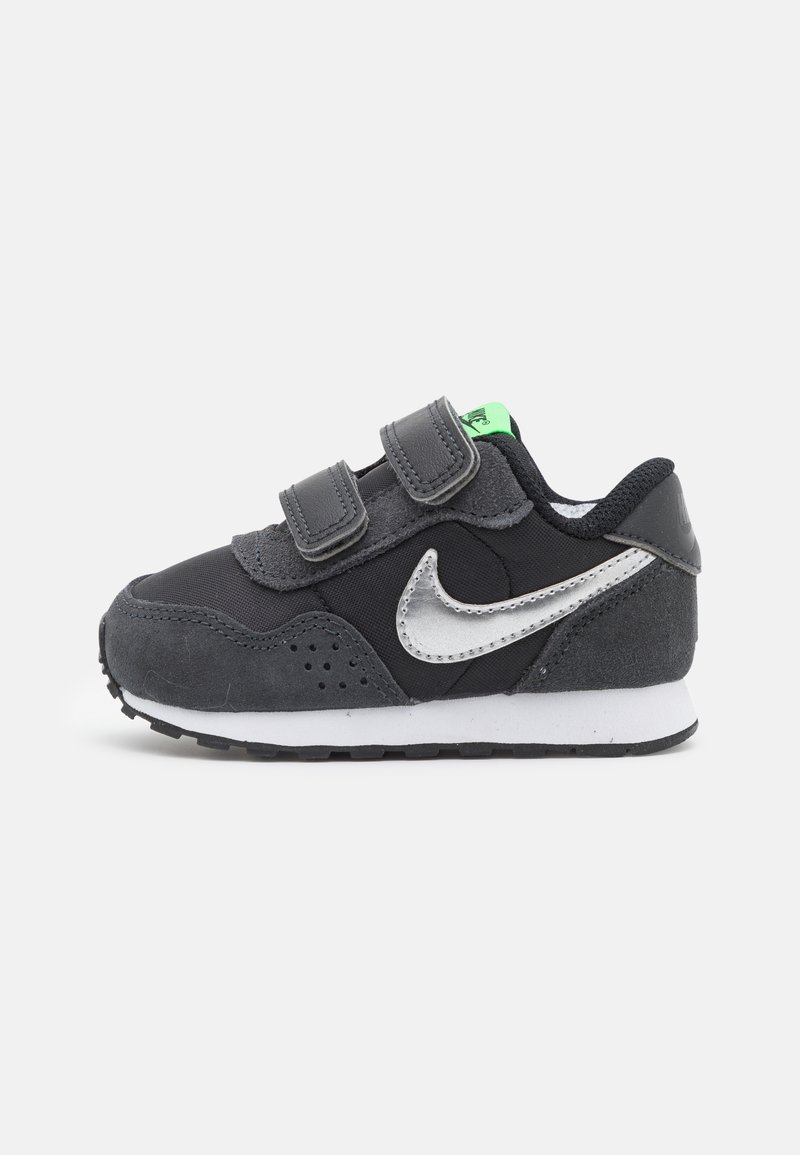 Baskets pour tout-petit noires et grises avec un swoosh Nike blanc, un onglet vert au talon et deux bandes auto-agrippantes sur fond blanc.