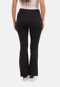 Pantaloni neri svasati con una texture liscia e vita aderente. Presentano una vita con passanti per la cintura e sottili dettagli di cucitura.