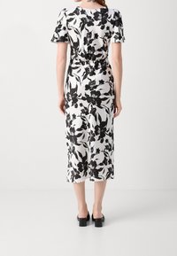 Robe midi florale en blanc et noir, avec des manches courtes, une taille cintrée, une jupe fluide et une texture lisse. Sandales à talons blocs noires.