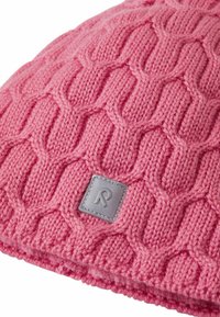 Knitted pink beanie featuring a textured cable pattern, with a soft fabric and a small gray patch displaying the letter “R.”