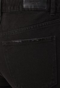 Jeans de mezclilla negra con un tejido texturizado, ajuste ceñido, bolsillo trasero con un leve desgaste y una etiqueta de cuero con la marca.