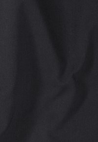 Tissu noir avec un motif en sergé diagonal et des plis subtils créant des ombres douces et des reflets.