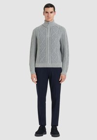 Maglione grigio lavorato a maglia con collo alto, caratterizzato da un motivo a rombi, abbinato a pantaloni scuri e scarpe nere. Design elegante e dettagliato.