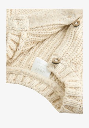 Pull pour bébé de couleur crème en tricot avec une texture côtelée et des boutons en bois, avec une étiquette marquée "NEXT BABY" et des détails texturés.