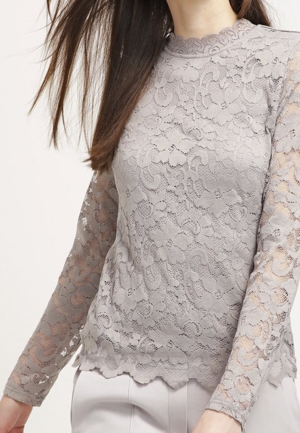 Lys grå blondebluse med lange ærmer, scalloped kant og blomstermønster. Har en rund halsudskæring med delikat detaljer.