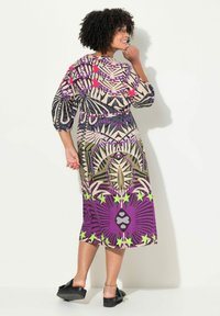 Bunt gemustertes Kleid mit floralen und abstrakten Motiven; verfügt über Dreiviertelärmel, einen elastischen Bund und eine fließende Silhouette.
