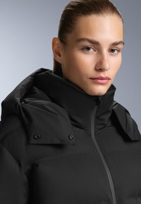 Crna zimska jakna s visokim ovratnikom, dugmadi na ramenima i glatkom, mat teksturom. Dizajnirana za toplinu i udobnost.