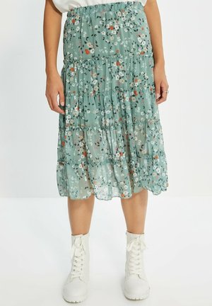 Jupe midi florale en vert clair, fabriquée en tissu superposé et transparent. Présente des fleurs blanches, orange et rose avec des feuilles subtiles. Taille élastique.