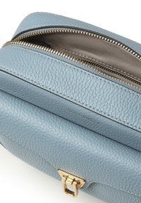 Borsa in pelle azzurro chiaro con finitura testurizzata, cerniera dorata e dettaglio con fermaglio. Si apre per rivelare una fodera interna liscia color beige.