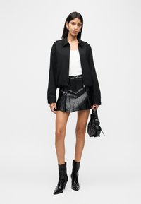 Μαύρο μπουφάν τύπου μπόμερ με φερμουάρ, λευκό εφαρμοστό τοπ, γυαλιστερή μαύρη δερμάτινη φούστα με πλισέ σχέδιο και γυαλιστερά μαύρα μποτάκια μέχρι τον αστράγαλο.