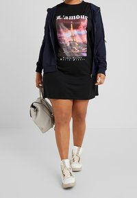 Černé tričko s grafikou Eiffelovy věže a bílým textem, doplněné černou sukní. Celkový vzhled dotváří námořnická modrá mikina na zip a bílé platformové tenisky.