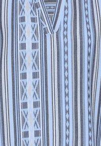 Chemise bleu clair tissée avec des rayures horizontales et verticales en bleu foncé, noir et crème. Motif géométrique centré ajoutant du détail.