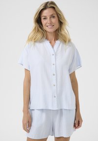 Completo loungewear blu chiaro in due pezzi con top button-up a maniche corte e orlo in pizzo, abbinato a pantaloni corti coordinate. Tessuto morbido e texturizzato.
