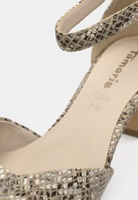 Sandale à talons hauts beige avec une tige tissée texturée présentant un motif en grille. Bride de cheville ajustable et doublure intérieure lisse.