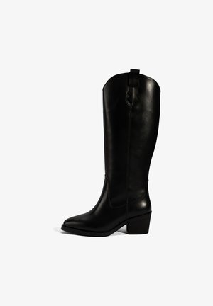 Zwarte leren kniehoge laars met een gladde textuur, spitse neus en een blokhak. Beschikt over een decoratieve golfrand bovenaan en zijsteeksels.