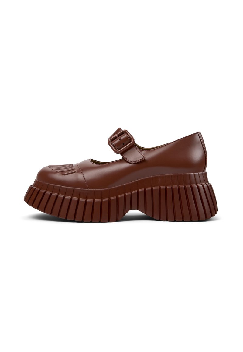 Chaussure Mary Jane en cuir verni marron avec un bout rond, une bride à boucle et une semelle épaisse et cannelée. La texture est lisse et brillante.