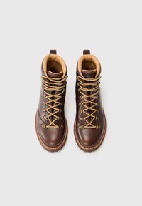 Pair of brown leather hiking boots with tan padded collars and yellow-brown laces on light grey background.