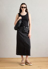 Black tank top, black denim maxi skirt, black handbag with pleated design, beige platform sandals; smooth textures and fitted shapes.