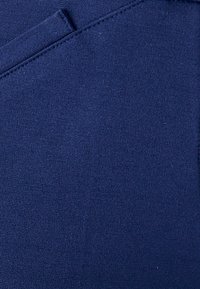 Marineblauwe stof met een gladde textuur, voorzien van subtiele stikseldetails en een kleine open pocket aan de rechterkant.