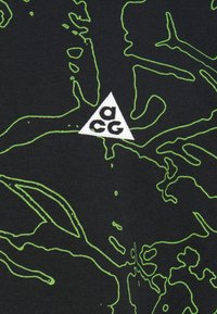 Μαύρο βαμβακερό μπλουζάκι με πράσινο γραμμικό σχέδιο και μικρό λευκό τρίγωνο λογότυπο στο στήθος με τα γράμματα "acg" μαύρα.