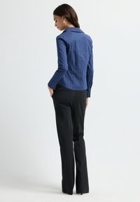 Blazer fitted a righe navy con colletto e maniche lunghe, abbinato a pantaloni neri su misura, visto da dietro. Texture liscia.