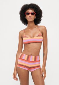 Csíkos bikini szett narancssárga, rózsaszín és barna árnyalatokban, bordázott textúrával. A szett tartalmaz egy bralette fazonú felsőt és magas derékú sortot, vékony pántokkal.