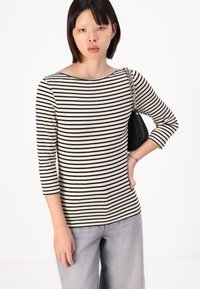 Svart og hvit stripete langermet skjorte med båthals. Bært med lysegrå jeans og en svart håndveske med kjedestropp.