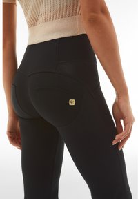 Leggings negros con una textura suave, que presentan costuras curvas y un pequeño logo en el bolsillo trasero. Ajuste de altura media.