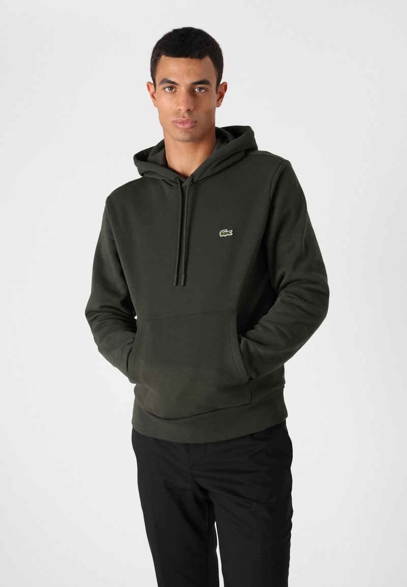 Hoodie vert foncé en matériau doux, avec une poche kangourou, un capuchon avec cordon de serrage et le logo Lacoste sur la poitrine.