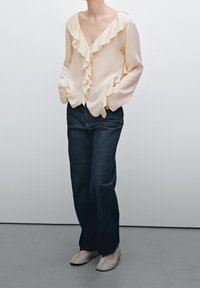 Blusa di raso rosa chiaro con scollatura a V arricciata, maniche lunghe, abbinata a jeans a gamba dritta blu scuro e scarpe slip-on grigie.