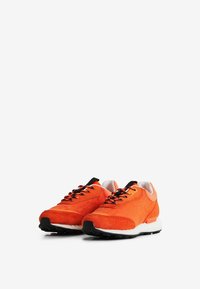 Scarpe da atletica arancioni con tessuto texture, dettagli in suede, lacci neri e una suola intermedia bianca. Un design elegante e moderno.