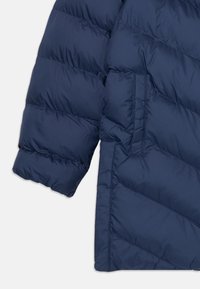 Casaco puffer azul marinho com um design acolchoado, costura visível e um bolso lateral. Textura suave com um acabamento ligeiramente brilhante.