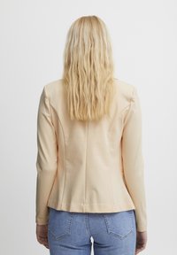 Růžový sako s dlouhými rukávy, hladkým povrchem, strukturovanými rameny a zadním záhybem, nošené přes modré džíny.