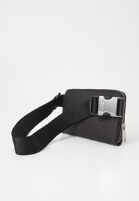 Zwarte stoffen portemonnee met een zilveren sluiting en rits. Beschikt over een brede, verstelbare schouderband van glad nylon. Minimalistisch ontwerp.