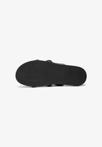 Black rubber shoe sole features a textured pattern, rounded edges, and minimal heel. Surface is smooth with a matte finish.