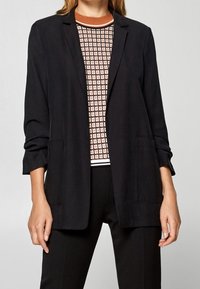 Svart kavaj med avslappnad passform, långa ärmar och två framfickor. Tillsammans med en mönstrad topp med rutmönster och orange inslag.