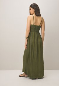 Pitkä oliivinvihreä mekko, jossa on kirjailtu yläosa ja ohuet olkaimet. Mekossa on liukuva siluetti ja kevyttä, tekstuuripintaista kangasta.