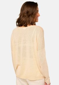 Pull en tricot pêche clair avec une coupe décontractée, des manches longues et une texture douce. Présente un décolleté large et des épaules tombantes.