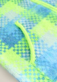 Detailný záber na chlpatu tkaninu s modro a neónovo žltým kockovaným vzorom a neónovo žltým okrajom pozdĺž zakrivenej švy.