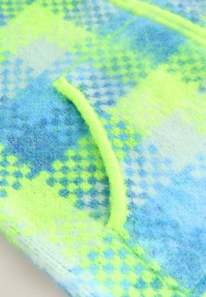 Közelkép bolyhos anyagról kék és neon sárga kockás mintával, neon sárga szegéllyel egy ívelt varrás mentén.