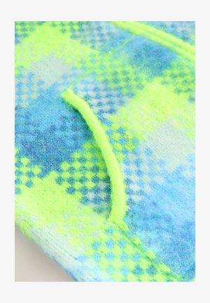 Detailaufnahme von flauschigem Stoff mit einem karierter blau und neongelben Muster und neongelber Einfassung entlang einer gebogenen Naht.