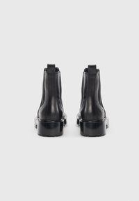Black leather ankle boots with a smooth finish, featuring elastic side panels and thick rubber soles. Minimalist design with a reinforced heel.