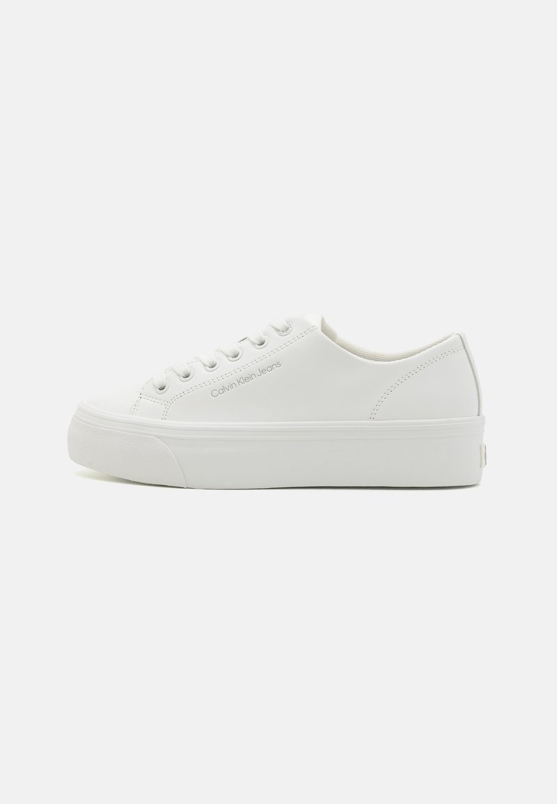 Hvite lave sneakers laget av glatt materiale, med snøring, flat såle og subtil merkevare på siden. Enkelt og minimalistisk design.