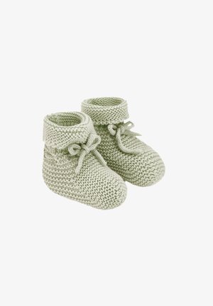 Chaussons de bébé tricotés doux vert clair avec revers pliés et nœuds attachés sur fond blanc.