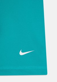 Turkusowa koszulka sportowa Nike z białym logo, gładką teksturą i krótkim, prostym dołem z widocznymi detalami szwów.