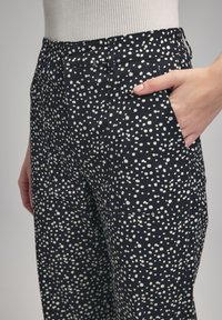 Zwarte broek met witte stippen, met een hoge taille, voorkruidtjes en een rechte pijp ontwerp. Gemaakt van textuurstof.